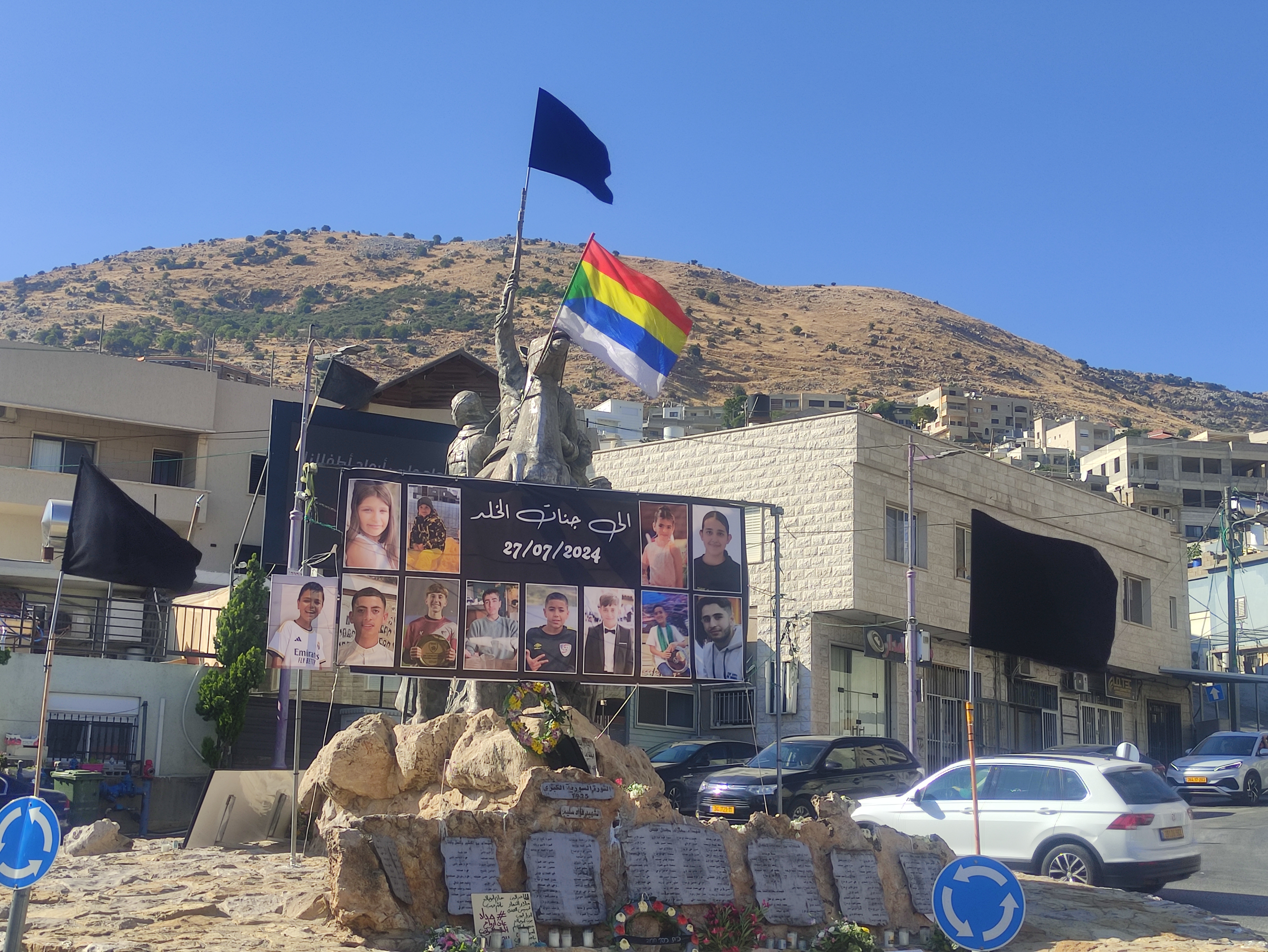 A black flag of mourning and the Druze flag at the monument in Majdal Shams, along with photos of the victims killed
